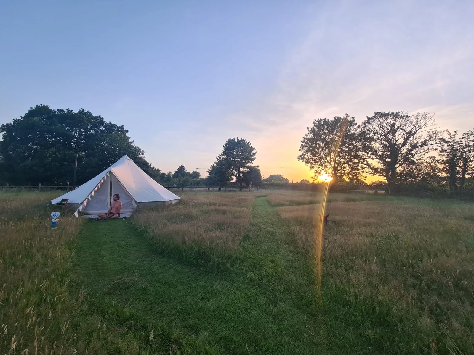 Canvas bell tent beside a path through the meadow at sunset